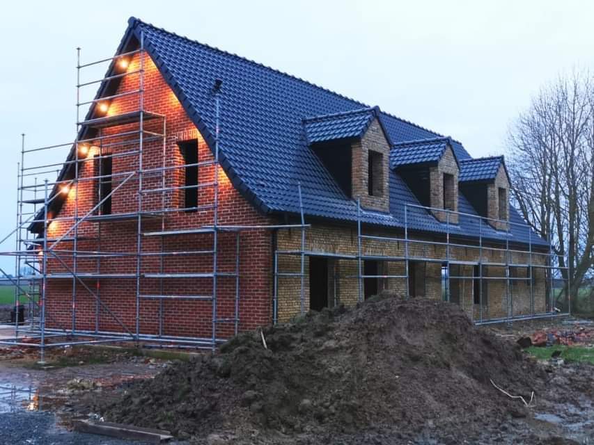 Maison en brique, toiture sombre et échafaudage installé en façade.