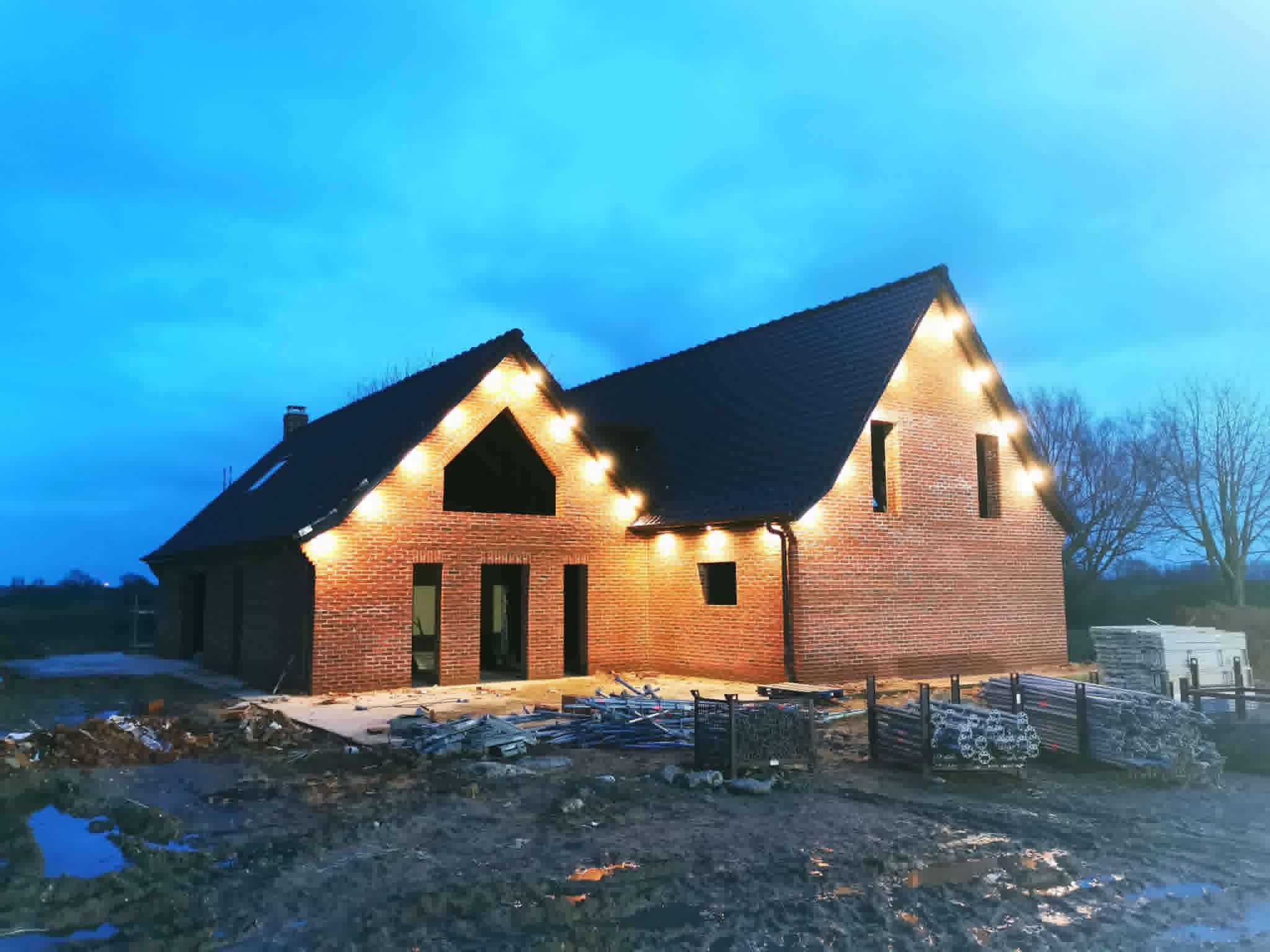 Maison en brique avec couverture sombre terminée, éclairée à la tombée du jour.