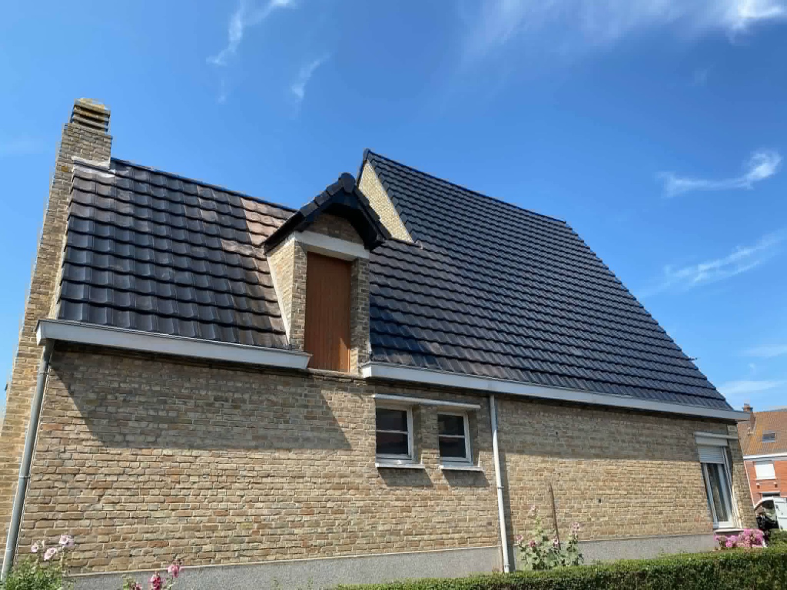 Maison en brique avec une couverture sombre terminée et deux fenêtres de toit.