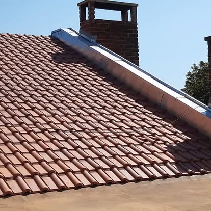 Vue rapprochée d'une toiture en tuiles avec raccord de cheminée métallique.
